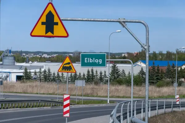 Uwaga na skrzyżowanie z drogą podporządkowaną i przejazd kolejowy. Znak "Elbląg" zaprasza do miasta.