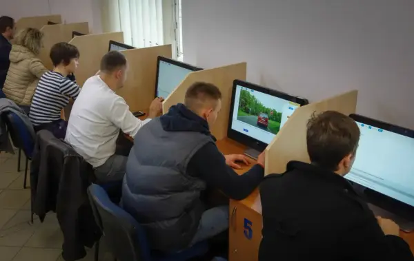 Ludzie siedzą przy komputerach, rozwiązując testy. To miejsce, gdzie można sprawdzić, kiedy można zdawać egzamin teoretyczny na prawo jazdy.